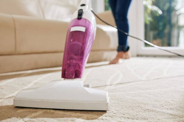 Close-up image of woman vacuum cleaning carpet in main room of her house - 写真・画像