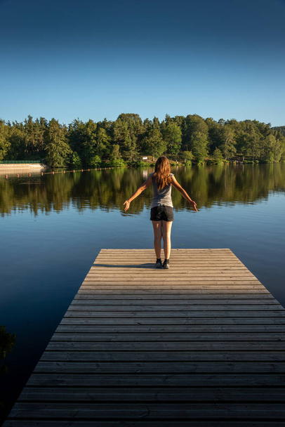young woman stretching at the end of a wooden jetty in the evening ,concept free spirit. - Photo, Image