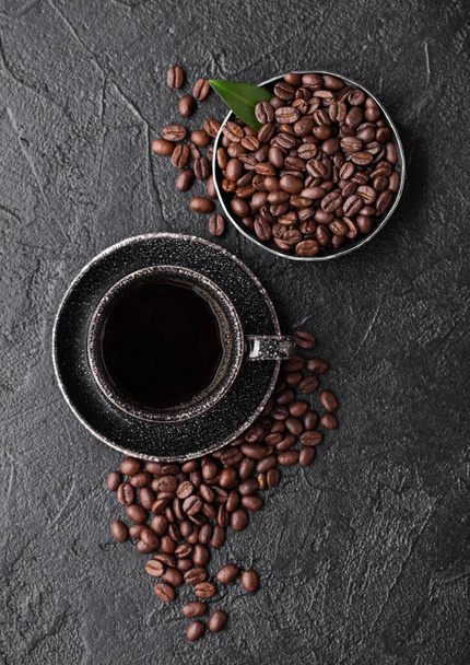 Cup of fresh raw organic coffee with beans and coffee tree leaf on black background. Black ceramic mug.  - Foto, afbeelding