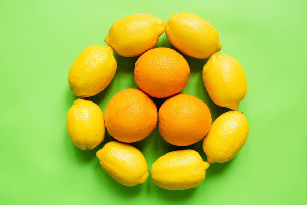 top view of ripe lemons and oranges arranged in circle on green background - Fotografie, Obrázek