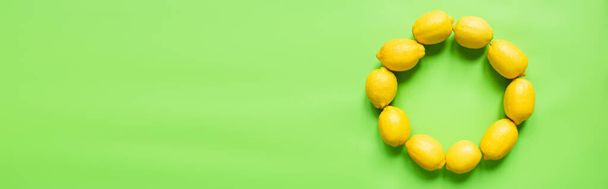 shora pohled na zralé žluté citrony uspořádané v kulatém prázdném rámu na zeleném pozadí, panoramatická orientace - Fotografie, Obrázek
