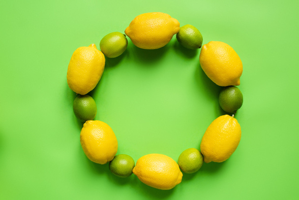 top view of ripe lemons and limes arranged in round empty frame on green background - Foto, Bild