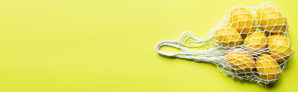 top view of ripe whole lemons in string bag on yellow background, panoramic crop - Fotografie, Obrázek