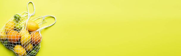 vista superior de cítricos enteros maduros en bolsa de hilo sobre fondo amarillo, cultivo panorámico
 - Foto, Imagen