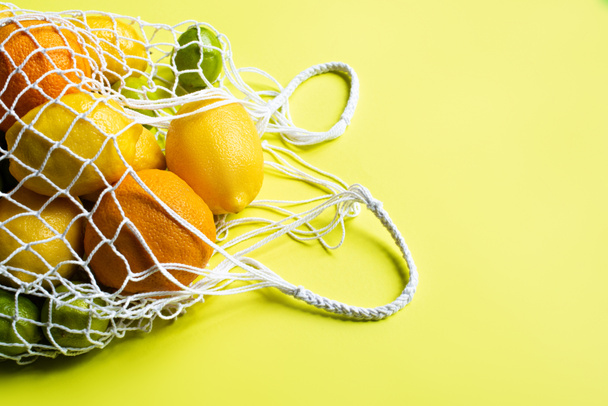 ripe whole citrus fruits in string bag on yellow background - Fotografie, Obrázek