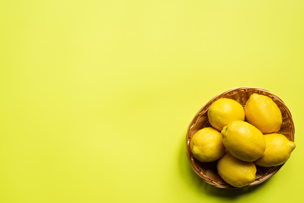 top view of ripe lemons in wicker basket on colorful background - Photo, image