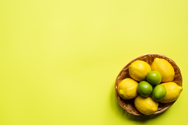 top view of ripe limes and lemons in wicker basket on colorful background - Foto, Bild