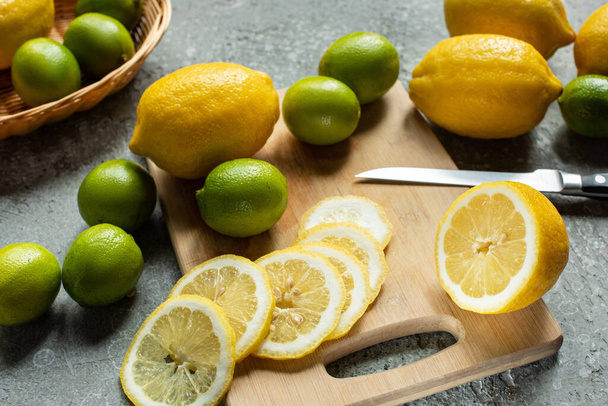 ripe yellow lemons and limes on wooden cutting board with knife on concrete textured surface - Fotó, kép