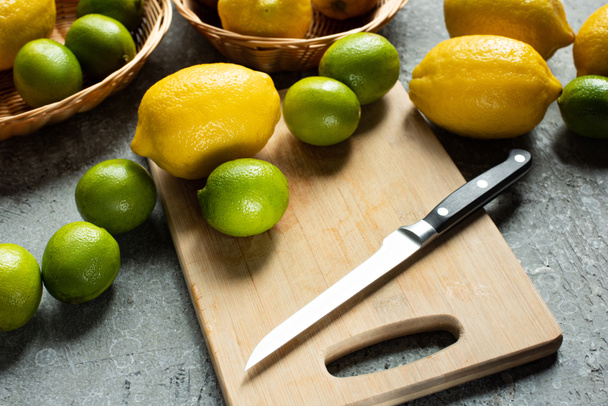 ripe yellow lemons and limes on wooden cutting board with knife on concrete textured surface - Foto, Bild