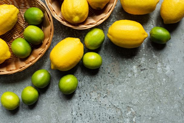 top view of ripe yellow lemons and green limes in wicker baskets on concrete textured surface - Foto, Bild