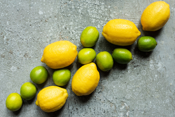 top view of ripe yellow lemons and green limes on concrete textured surface - Fotó, kép