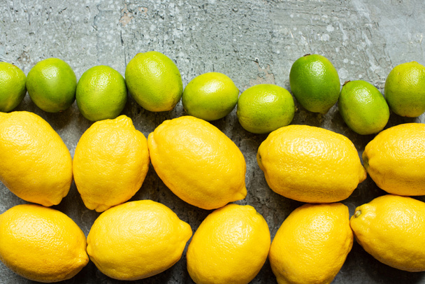 Beton desenli yüzeyde olgun sarı limonların ve yeşil limonların üst görüntüsü - Fotoğraf, Görsel