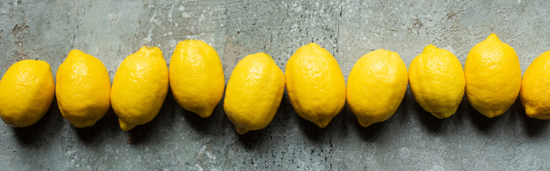 vista dall'alto di limoni gialli maturi in fila su superficie testurizzata di cemento, coltura panoramica - Foto, immagini
