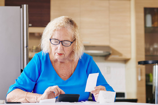Pensive senior woman in glasses checking bills and handles bookkeeping - Fotografie, Obrázek