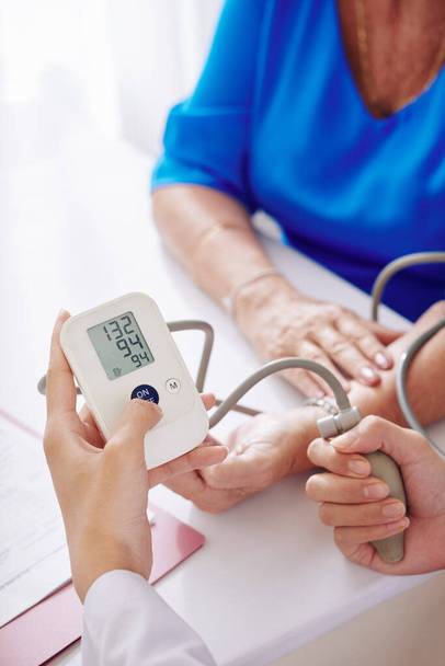 Руки лікаря загального профілю з використанням електронного тонометра при перевірці артеріального тиску старшої жінки
 - Фото, зображення