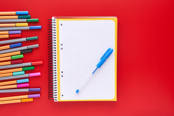 Farbige Marker und ein Notizbuch auf rotem Hintergrund. Zurück zu Schulkonzept und Handwerk. - Foto, Bild