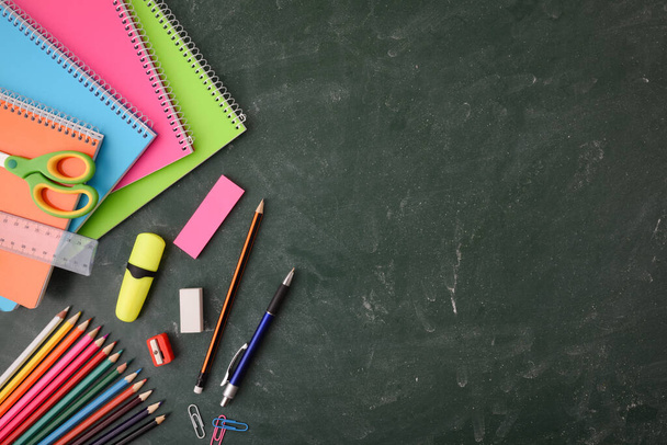 School educational supplies such as notebooks, colored pencils and others on green blackboard. Top view. - Photo, Image