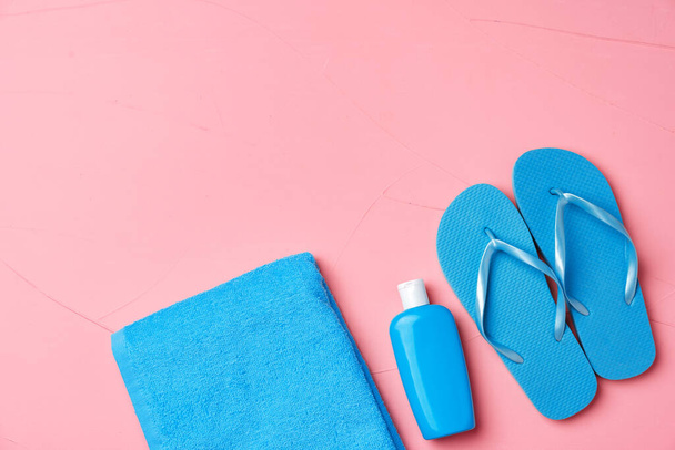 Blue towel, cosmetic bottle with sunscreen cream and flip-flops on pink background - Φωτογραφία, εικόνα