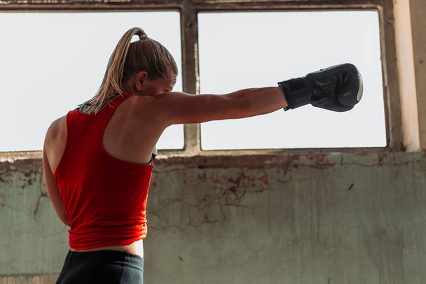 Beautiful fit blond girl in boxing training. Active lifestyle. Indoor shot by the window, old building. Copy space, space for writing - Photo, image