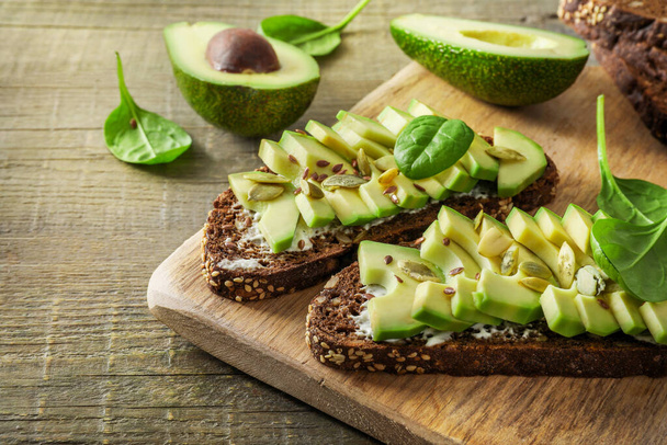 Seasoned avocado sandwiches on wooden cutting board on wooden background. - Photo, image