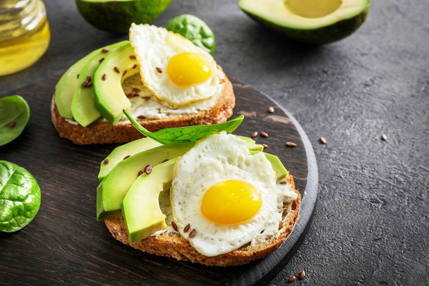 Avocado sandwiches with fried eggs and spinach leaves on wooden cutting board on dark background. - Foto, Imagen