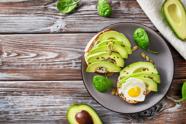 Avocado sandwiches with fried eggs and spinach leaves in plate on wooden background. Top view. - Фото, изображение
