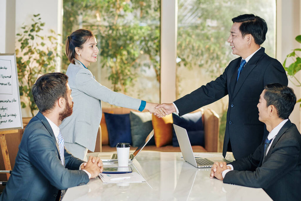 Lachende Vietnamese zakenpartners schudden handen na productieve vergadering - Foto, afbeelding