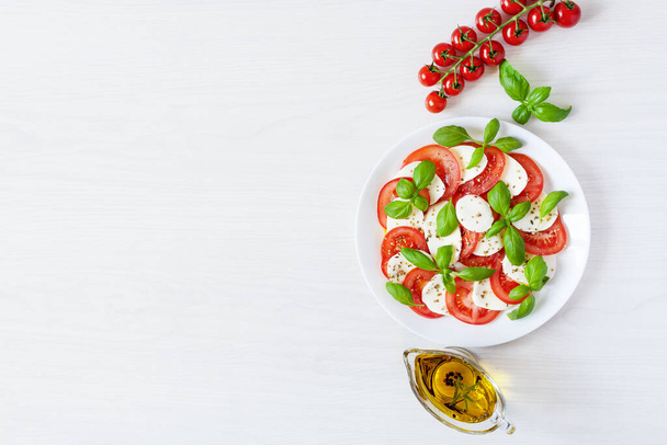 Caprese salade met mozzarela, tomaten, verse olijfolie en basilicum op witte achtergrond bovenaanzicht. Heerlijke Italiaanse veganistische salade. - Foto, afbeelding
