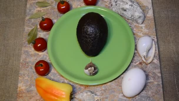 sur une assiette verte avocat, ail et environs : légumes, œufs de poulet, coquillages, tomates cerises, poivron doux, feuilles de laurier sur une surface en marbre - Séquence, vidéo