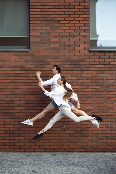 Jumping young couple in front of buildings, on the run in jump high - Фото, зображення