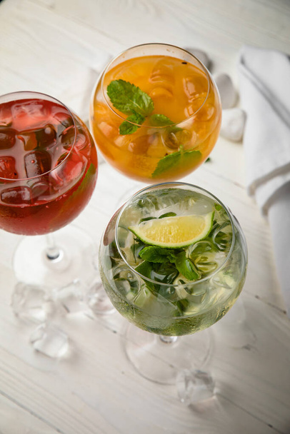 Assorted cold cocktails - mojito, orange and raspberry. On a wooden, white table - Fotó, kép