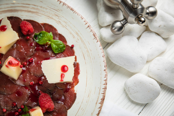 veal carpaccio with parmesan and pomegranate sauce. On a white wooden table. - 写真・画像