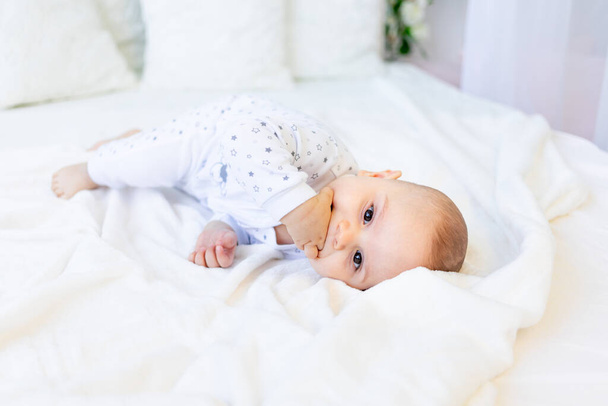 μικρό αγόρι 6 μηνών ξαπλωμένο στο κρεβάτι με πιτζάμες και πιπίλισμα το δάχτυλό του, μωρό πριν πάει για ύπνο, θέση για κείμενο - Φωτογραφία, εικόνα