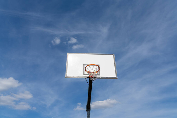 geïsoleerde weergave van een basketbalring en backboard onder een expressieve blauwe lucht met kopieerruimte - Foto, afbeelding