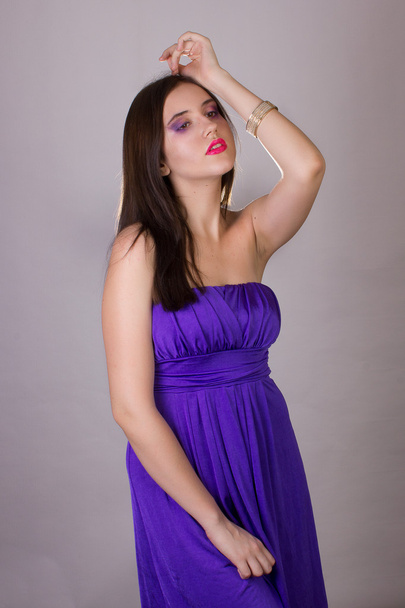 Emotional studio portrait of a beautiful brunette girl in a cocktail dress and lilac bright evening makeup with pink lips - Foto, Bild