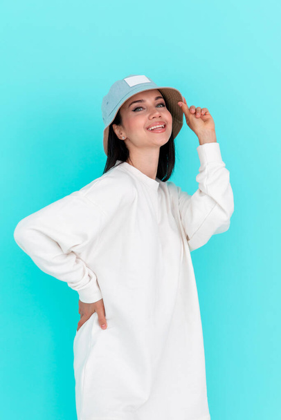 Beautiful girl model in white hoody in hat on a blue background - Fotó, kép