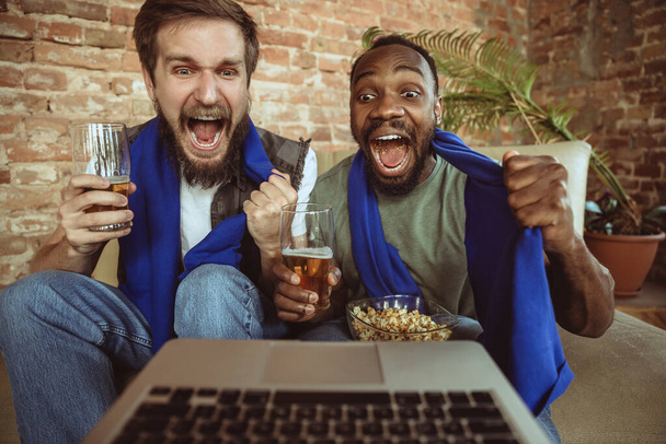 Excited football fans watching sport match at home, remote support of favourite team during coronavirus pandemic outbreak - 写真・画像
