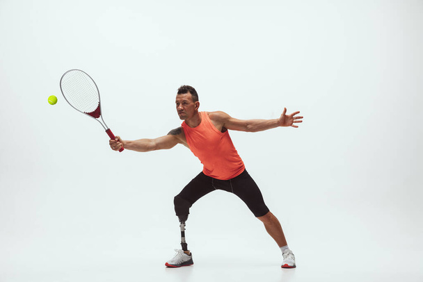 Athlete with disabilities or amputee isolated on white studio background. Professional male tennis player with leg prosthesis training and practicing in studio. - Fotografie, Obrázek