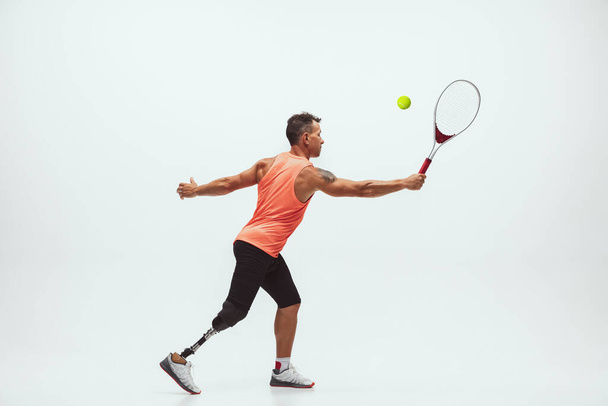 Athlete with disabilities or amputee isolated on white studio background. Professional male tennis player with leg prosthesis training and practicing in studio. - Foto, imagen