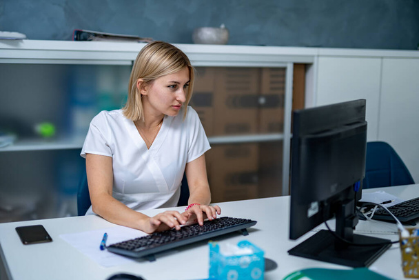 Serious female doctor near computer. Typing diagnosis on keyboard. - Foto, imagen
