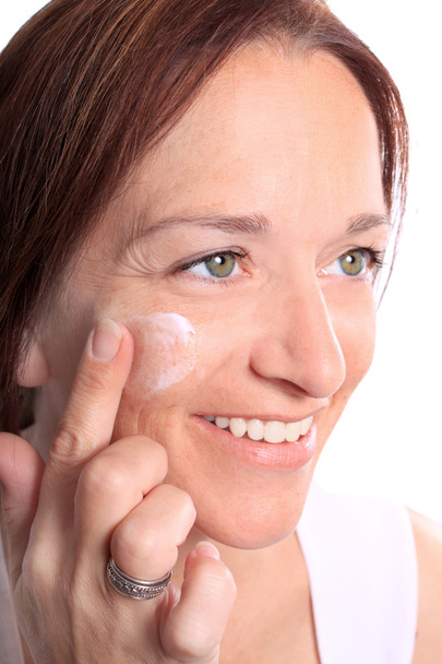 Доросла жінка наносить крем на обличчя
 - Фото, зображення