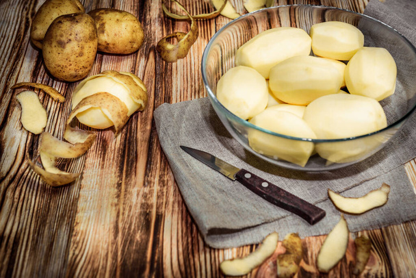 Raw peeled sliced potato, pile of potatoes and knife on rustic wooden table.  - Photo, Image