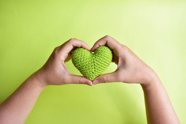 Una donna che tiene un cuore verde all'uncinetto sulla sua mano in sfondo verde pastello, simbolo di amore e pace, forma di amore cuore, San Valentino, romanticismo, amicizia, partnership, regalo, stile di vita verde - Foto, immagini