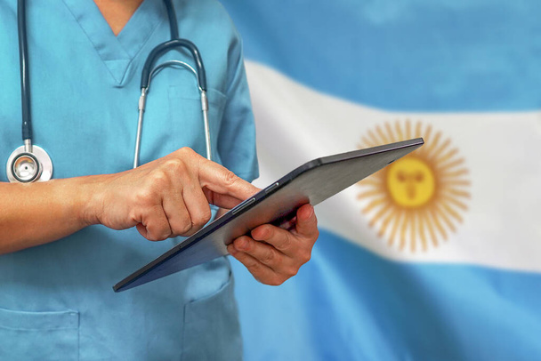 Chirurgo o medico che utilizza un tablet digitale sullo sfondo della bandiera argentina. Apparecchiature mediche o rete medica, tecnologia e diagnostica in Argentina. - Foto, immagini