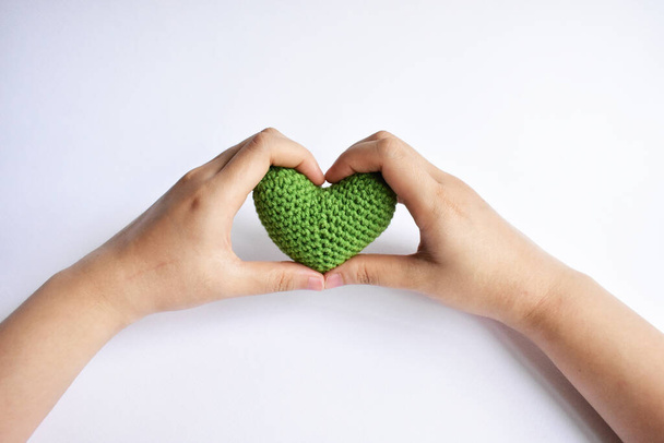 Uma mulher segurando um coração de crochê verde em sua mão em fundo branco, símbolo de amor e paz, forma de coração de amor, vírus corona, amor médico, curar o mundo
 - Foto, Imagem