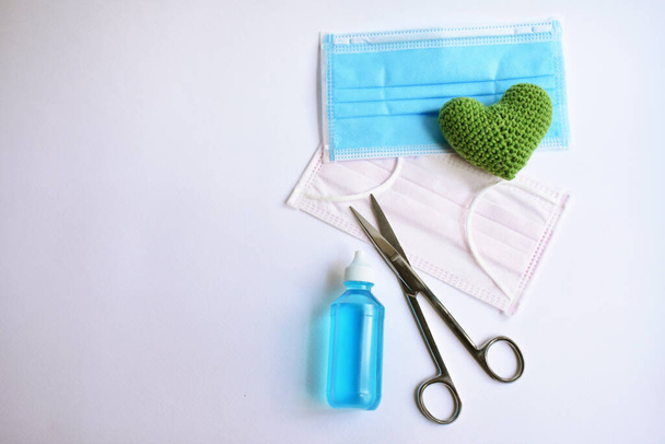First aid objects for Corona virus protection: alcohol to wash hands, medical face masks, green crochet heart, medical scissors, white background, Corona virus Disease, hospital, washing hands - Photo, Image