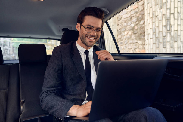 Отличные решения каждый день. Уверенный молодой бизнесмен, работающий над своим ноутбуком, сидя в машине
. - Фото, изображение