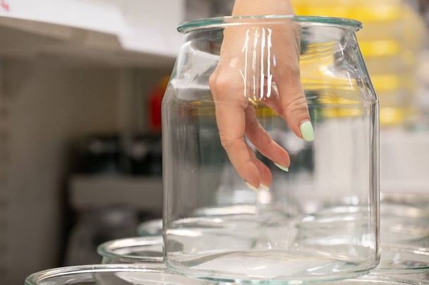 Female hand in an empty glass jar. A row of transparent kitchen containers in a store. - Foto, Bild