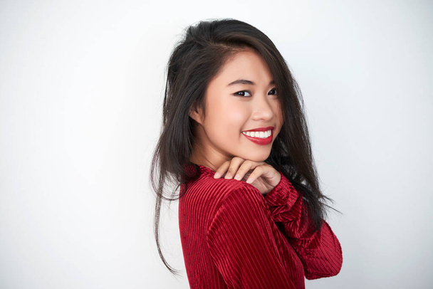 Horizontaal medium close-up portret van charmante Aziatische vrouw met donkerrood bovenblad en wijnrode lippenstift kijkend naar camera glimlachend, witte achtergrond, kopieerruimte - Foto, afbeelding