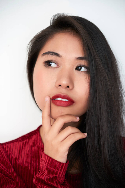 Vertical close-up studio portrait shot of beautiful young Asian woman with dark-red lips thinking of something, white background - Fotó, kép